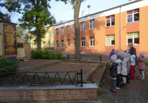 Grupa dzieci wraz z panią Arletą stoi pod pomnikiem poległych podczas II wojny światowe.